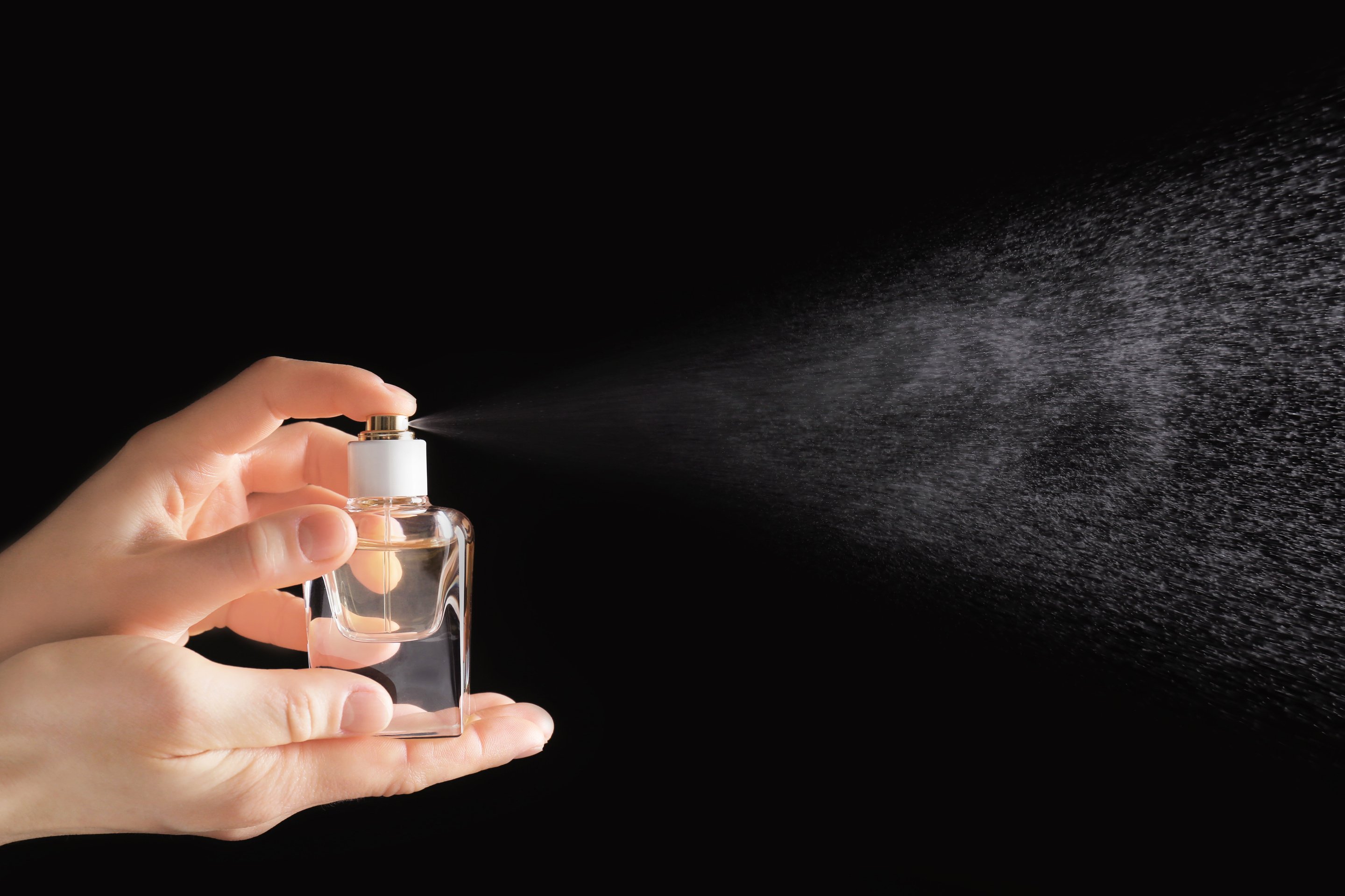 Person Spraying Perfume Against a Black Background